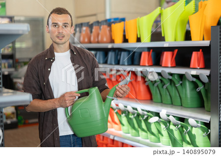 Amateur gardener guy selects watering can for hobby in greenhouse flower-bed Amateur gardener guy selects watering can for hobby in greenhouse flower-bed 140895079