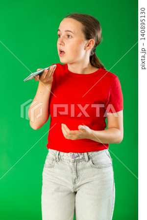 Teenage girl in red T-shirt and jeans emotionally records an audio message on mobile phone. Chroma key compositing 140895130