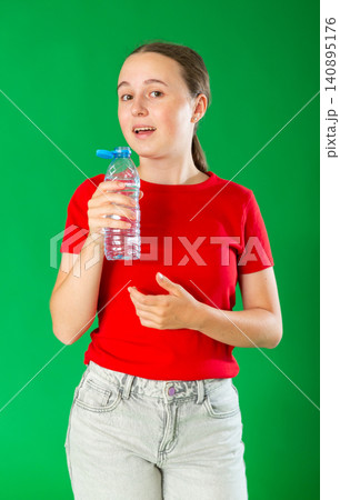 Teenage girl in red T-shirt and jeans drinks water from plastic bottle on green background. Chroma key compositing Teenage girl in red T-shirt and jeans drinks water from plastic bottle on green background. Chroma key compositing 140895176
