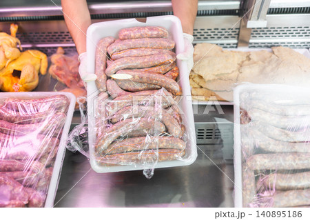 Close-up sellers hands hold put add tray with sausages to glass showcase refrigerator Close-up sellers hands hold put add tray with sausages to glass showcase refrigerator 140895186