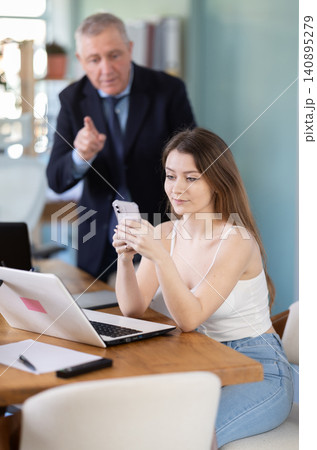 Senior businessman complains to subordinate about her talking on her mobile phone while working in office Senior businessman complains to subordinate about her talking on her mobile phone while working in office 140895279