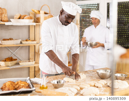 African American baker cutting and shaping dough in professional bakery African American baker cutting and shaping dough in professional bakery 140895309