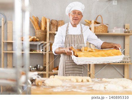 Bakery mature man employee holds basket of ready-made baguettes. Bakery mature man employee holds basket of ready-made baguettes. 140895310