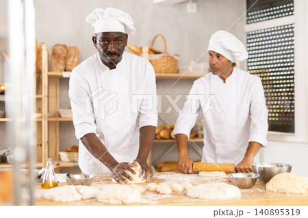 Two male bakers kneading dough and rolling it out Two male bakers kneading dough and rolling it out 140895319