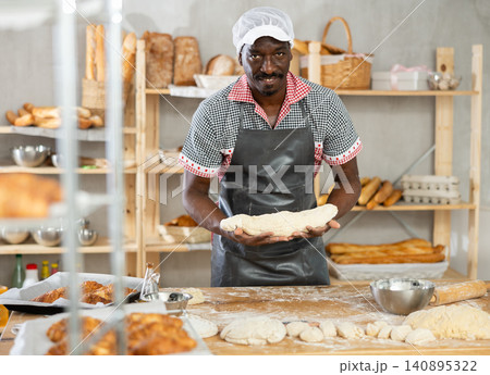 Professional male baker prepares raw yeast dough in bakery, shaping it into baguette Professional male baker prepares raw yeast dough in bakery, shaping it into baguette 140895322