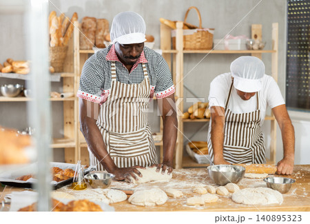 Two male bakers kneading dough and rolling it out Two male bakers kneading dough and rolling it out 140895323