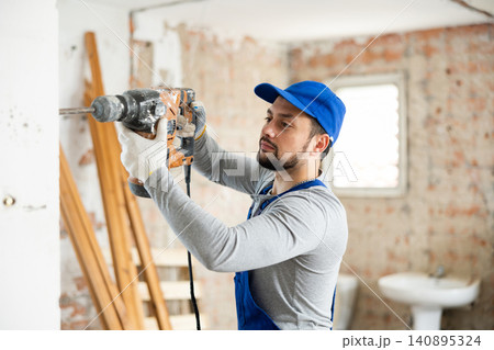 Professional builder drilling hole in wall with perforator in repairable room Professional builder drilling hole in wall with perforator in repairable room 140895324