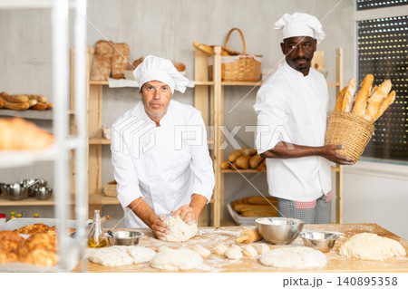 Two male bakers knead dough and put baked goods Two male bakers knead dough and put baked goods 140895358
