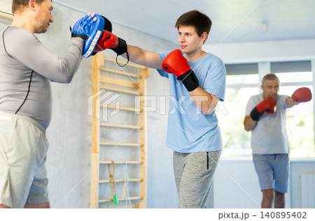 Guy in boxing gloves punching pads in hands of coach during workout 140895402