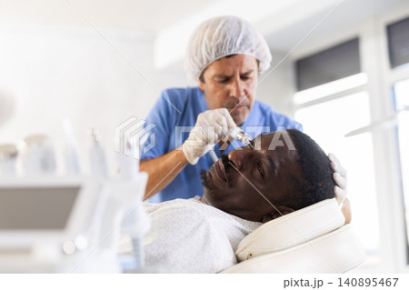 Male cosmetologist performs skin cleansing procedure for African man client with beauty machine 140895467