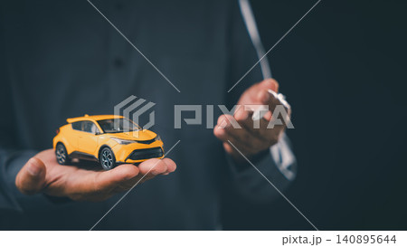 Dealership auto finance agent offers car buying loan approval and vehicle lease contract with insurance options while holding yellow toy car and pen against dark background Dealership auto finance agent offers car buying loan approval and vehicle lease contract with insurance options while holding yellow toy car and pen against dark background 140895644