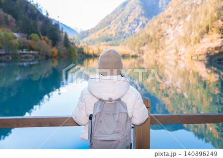 Happy woman traveler travel in jiuzhaigou national park in Sichuan, China. Tourist sightseeing Panda lake and snow mountain in Autumn season. Famous Landmark and Vacation near Chengdu, China 140896249
