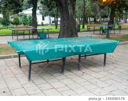 Ping pong tables covered with tarpaulin. Protect mouth from rain. End of summer concept in the park. sport in the park. holiday at the resort. 140896576