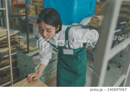 スーパーのバックヤードで腰を痛めた女性スタッフ スーパーのバックヤードで腰を痛めた女性スタッフ 140897067