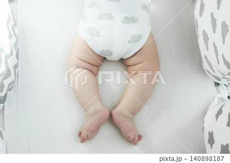Baby lying on bed with white bedding and patterned pillows Baby lying on bed with white bedding and patterned pillows 140898187
