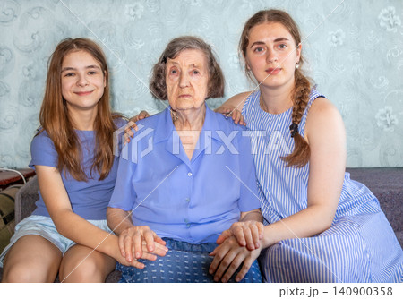 Grandmother with two granddaughters sitting on a couch showing family support and affection Grandmother with two granddaughters sitting on a couch showing family support and affection 140900358