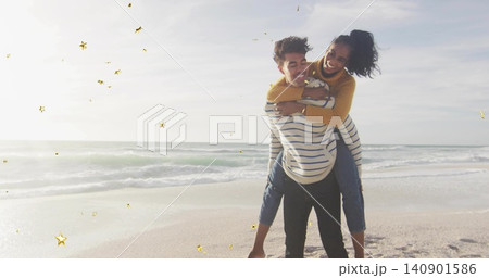 Carrying man carrying woman piggyback on beach shore in sweaters and jeans golden stars, copy space 140901586