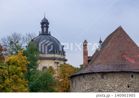 A view of an old European city featuring a grand dome and a rustic stone tower, surrounded by trees in fall colors A view of an old European city featuring a grand dome and a rustic stone tower, surrounded by trees in fall colors 140901985