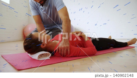 Therapist kneeling beside client in red top on pink mat in studio supporting chest with towel Therapist kneeling beside client in red top on pink mat in studio supporting chest with towel 140902148