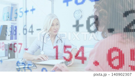 Consulting doctor taking notes at clinic desk with stethoscope and clipboard, patient in pink top 140902307
