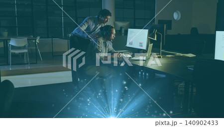 Reviewing coworkers in shirts leaning over laptop and monitor in open office with lamp, blue flare Reviewing coworkers in shirts leaning over laptop and monitor in open office with lamp, blue flare 140902433