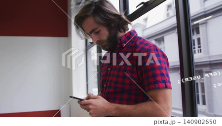 Standing man in red-navy check shirt using smartphone in office by window, with painted wall, tube Standing man in red-navy check shirt using smartphone in office by window, with painted wall, tube 140902650