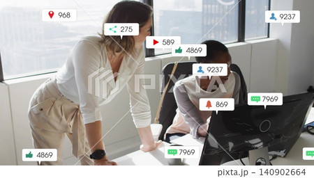 Reviewing women in office wear collaborating at office desk, with curved monitor and social badges 140902664
