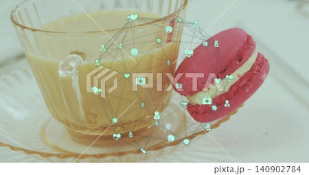 Displaying glass teacup holding pale beverage on tabletop, featuring pink macaron and teal overlay Displaying glass teacup holding pale beverage on tabletop, featuring pink macaron and teal overlay 140902784