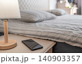 Black smartphone lying on a wooden nightstand next to a bed 140903357