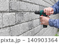 Close up of worker hand drilling into a gray brick wall with cordless electric screwdriver 140903364
