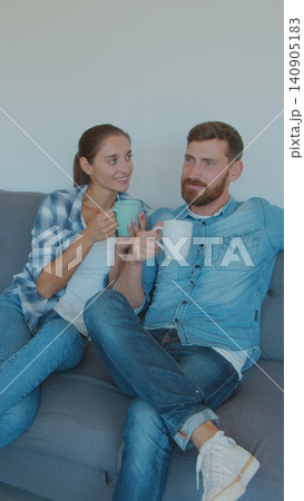 Vertical Video Panning waist-up shot of pleased smiling Caucasian husband and wife relaxing and drinking tea, sitting between cardboard boxes after house move. 140905183