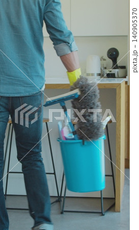 Vertical Video Man holding mop and plastic bucket with brushes, gloves and detergents in the kitchen. 140905370