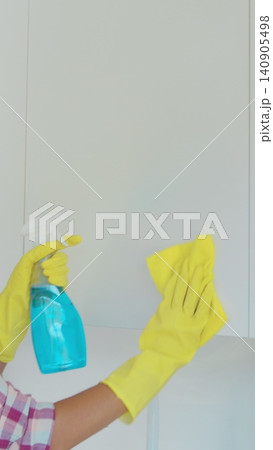 Vertical Video Woman's hand in a yellow rubber glove cleans the shiny surface of a modern plastic kitchen Cabinet with a cloth. The concept of spring cleaning and home work. Vertical Video Woman's hand in a yellow rubber glove cleans the shiny surface of a modern plastic kitchen Cabinet with a cloth. The concept of spring cleaning and home work. 140905498