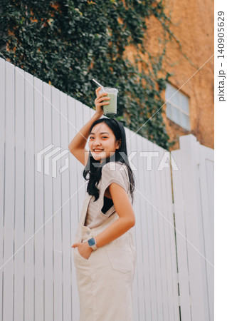 Young woman drinking iced coffee outside a chocolate shop 140905629