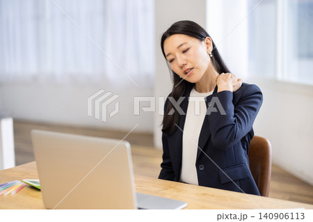 明るい窓辺でパソコンで作業しながら肩に触れて痛そうな若い日本人ビジネスウーマン 140906113