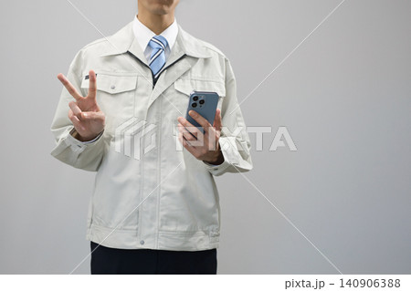 スマホを持ってVサインをする作業服の若い男性 スマホを持ってVサインをする作業服の若い男性 140906388