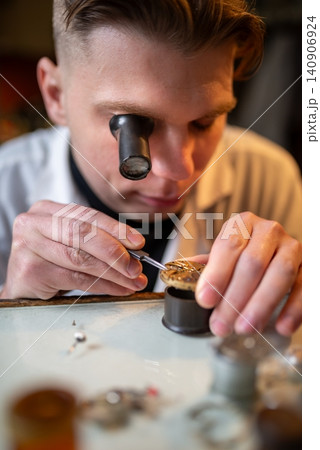 Watchmaker repairing mechanical watch movement under magnifying loupe with precise tools 140906924