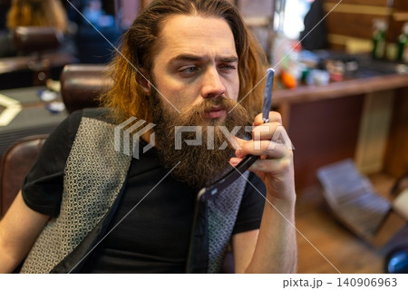 Long haired barber inspecting a straight razor blade while sitting Long haired barber inspecting a straight razor blade while sitting 140906963