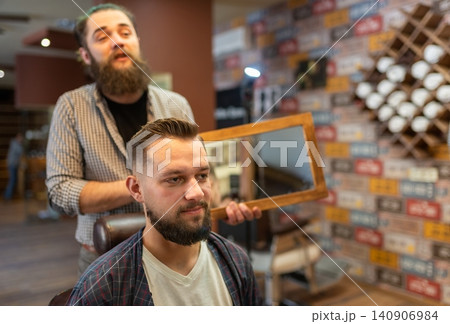 Client checking his fresh haircut in the mirror at a modern barbershop Client checking his fresh haircut in the mirror at a modern barbershop 140906984