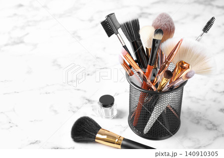 Set of professional makeup brushes in holder on white marble table Set of professional makeup brushes in holder on white marble table 140910305