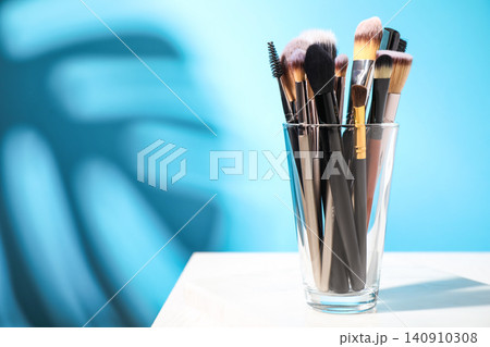 Set of professional makeup brushes in holder on table against blue background. Space for text Set of professional makeup brushes in holder on table against blue background. Space for text 140910308