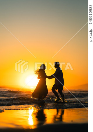 Couple dances at the beach during sunset on a warm evening near the water's edge in a joyful moment together Couple dances at the beach during sunset on a warm evening near the water's edge in a joyful moment together 140910988