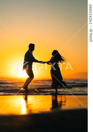 Couple holds hands and dances in shallow water during sunset at the beach Couple holds hands and dances in shallow water during sunset at the beach 140910989