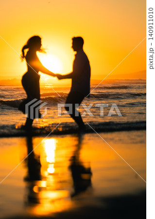 Couple plays on the beach during sunset and enjoys the warm light and waves while holding hands and smiling at each other Couple plays on the beach during sunset and enjoys the warm light and waves while holding hands and smiling at each other 140911010