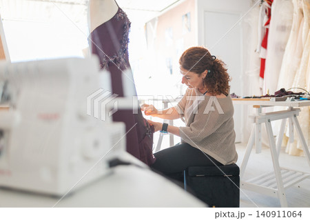 Female tailor creating custom gown in fashion atelier Female tailor creating custom gown in fashion atelier 140911064
