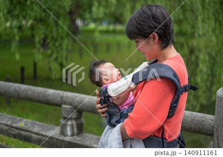 公園で抱っこ紐の赤ちゃんを見つめる母親 公園で抱っこ紐の赤ちゃんを見つめる母親 140911161