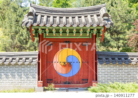 Brightly colored door at a traditional Korean gate surrounded by trees and stone walls during a sunny day 140911277