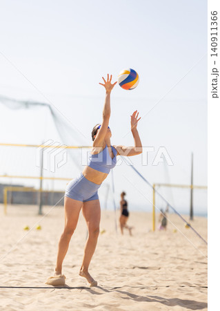 Volleyball player serves ball on beach court while others play in background Volleyball player serves ball on beach court while others play in background 140911366