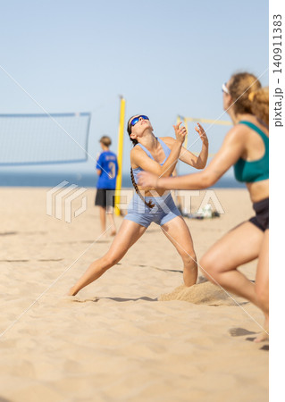 Beach volleyball match takes place under clear sky with athletes competing on warm sand near ocean waves Beach volleyball match takes place under clear sky with athletes competing on warm sand near ocean waves 140911383