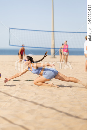 Young woman dives for volleyball during a game at a beach with players and a net in the background Young woman dives for volleyball during a game at a beach with players and a net in the background 140911413